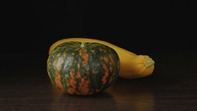 Pumpkin and squash are on the table. Autumn still life of vegetables. Green-orange pumpkin and yellow squash on a dark background. The camera moves smoothly past objects.