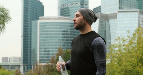 fitness man in a hat drinking from sport bottle during a workout pause. male athlete replenishing water balance after fitness workout. autumn. Relaxed fit girl drink water from bottle. Guy hydrating