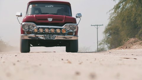 San Luis, Argentina - October 2021: An Old Red Ford F100 1960 Pickup Truck on a Rural Dirt Road. Low Angle View. 4K Resolution.
