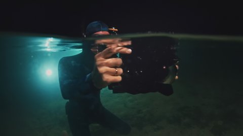 Underwater photographer in night lake. Young woman in wetsuit dives with underwater camera and takes pictures in the lake at night