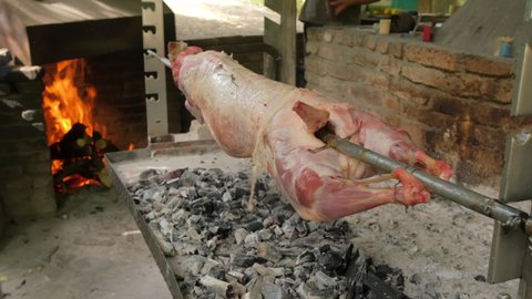 Spit roasting a whole lamb over hot coals. Rotating lamb cooking over an open fire in outdoor restaurant