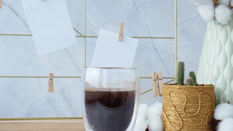 Woman add milk to Cup of coffee. Slow motion White home office room interior, bloggers workplace. Mood board with postcards and reminders mockup. Cotton branches in a vase, interior decoration
