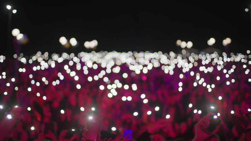 unrecognizable group of fans holding cell phones with flashlights in theirs hands in night time, atmosphere of concert out of focus Royalty-Free Stock Footage #1080494615