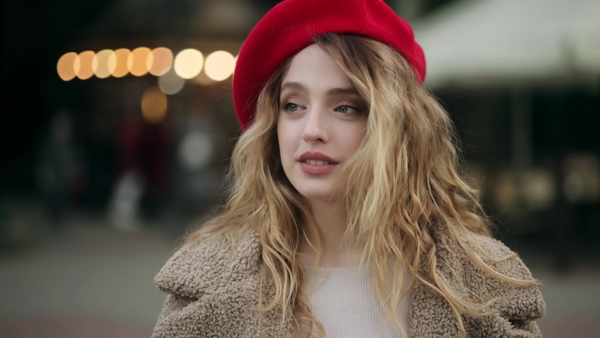 Portrait of young beautiful caucasian blond woman in red beret looking at the camera at the evening city. Close up of happy young girl smiling.