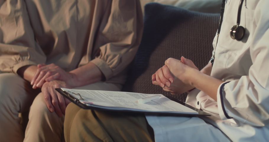 Checking pulse. Close-up female doctor in lab coat examining older patient at home for symptoms during house call visit.