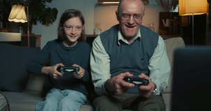 Happy 65-70 senior grandfather having fun playing console video game with joysticks against cute teen granddaughter girl