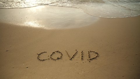 Covid 19 ​text on the sand on the beach. Waves from the sea erase the covid text. 
