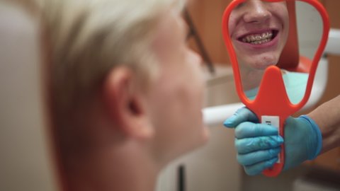 Teenager trying mouthguard and posing during consultation with orthodontist in clinic office spbd. Close-up view of handsome guy inserts transparent model over teeth and looks with smile, shows result