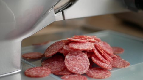Slicing a pepperoni sausage. A meat slicer at work. Cured dry sausage slices. Slicer machine in action