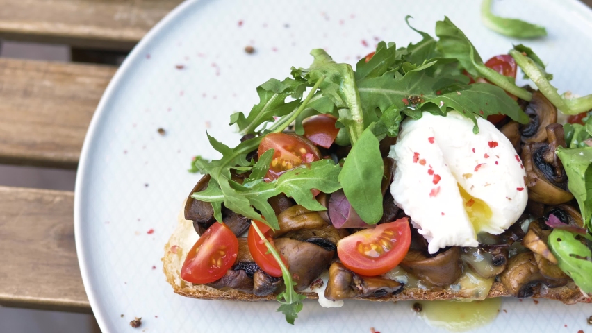 Woman hands cut canape with pouched egg mushrooms tomatoes and ruccola on piece of bread with knife and fork extreme closeup | Shutterstock HD Video #1080509648