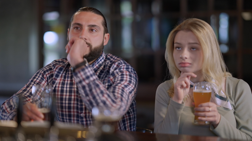 Bored girlfriend yawning sitting in pub with boyfriend watching football soccer match talking. Portrait of disinterested Caucasian young woman dating with enthusiastic man sports fan in bar indoors Royalty-Free Stock Footage #1080514970