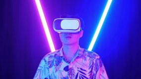Vr, Futuristic, Entertainment Concept. Excited Asian Man Using Virtual Reality Headset And Use Hand Slide With Neon Light At The Background
