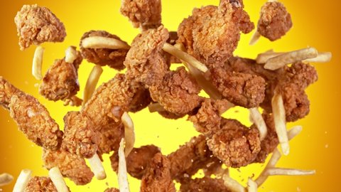 Super slow motion of flying fried chicken pieces with french fries isolated on golden background. Filmed on high speed cinema camera, 1000fps. Speed ramp effect.