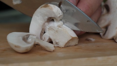 Close-Up Man Cutting Champignons on Wooden Cut Board. Diet Healthy Eating. Macro Shot Male Hands Cutting Champignon Mushroom By Knife on Wooden Board. Vegetarian Healthy Food. Diet Healthy Lifestyle.