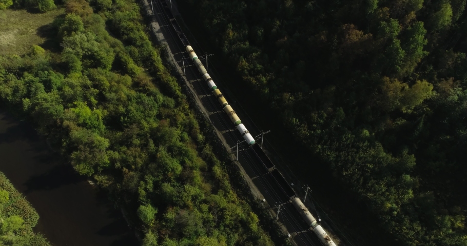Freight long train carries with oil tank and petrol carriages an electric locomotive by Trans Siberian railways under the rock and near mountain river. Aerial drone wide view at summer sunny day Royalty-Free Stock Footage #1080522998