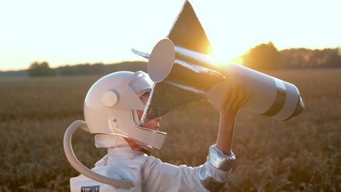 Little young happy cute child boy wearing astronaut uniform and helmet cosmonaut playing, launching toy rocket at sunset field, Space man, Kid dream flying, childhood, freedom, travel, future concept
