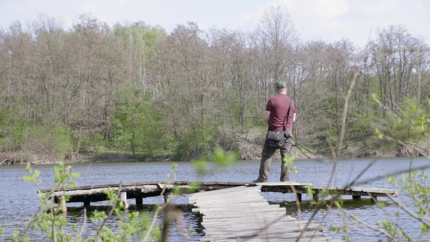 Wide shot fisherman catches fish while standing on a wooden bridge. Adult man with fishing rod