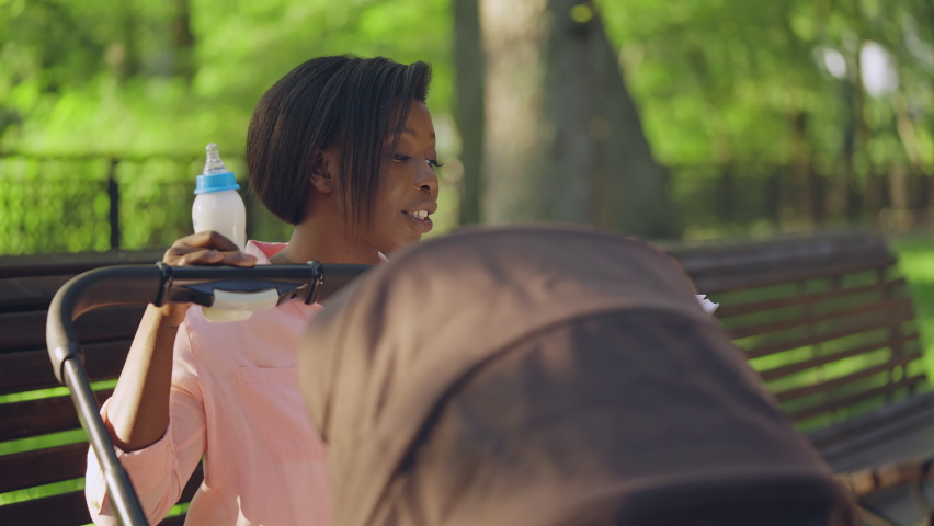 Smiling african american woman with feeding bottle reading to baby in park