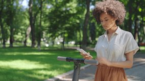 African-american woman renting electric scooter via smartphone app in park - Powered by Shutterstock - Get 15% off with code: PIKWIZARD15