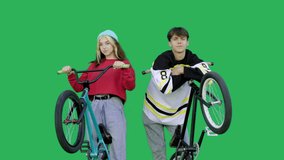 Young couple hold bicycles together over green background. Man and woman hold bmx bikes with rotated wheels have fun look at camera. Chroma key. 4k raw video footage