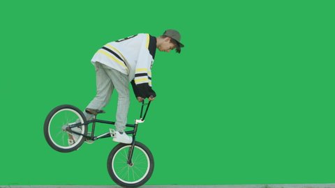 Extreme bmx guy biker wearing hockey jersey pedaling and jumping tricks over green screen background. Sporty young man rider have fun with bicycle. 4k raw video footage