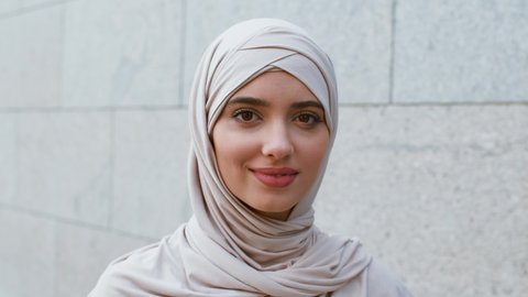 Middle eastern beauty. Close up outdoors portrait of carefree calm young muslim woman wearing hijab smiling to camera, posing outdoors, tracking shot, slow motion