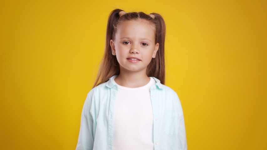 Like and approval. Studio portrait of cute little girl with two ponytails gesturing thumbs up with both hands and smiling to camera, orange background, slow motion Royalty-Free Stock Footage #1080528539