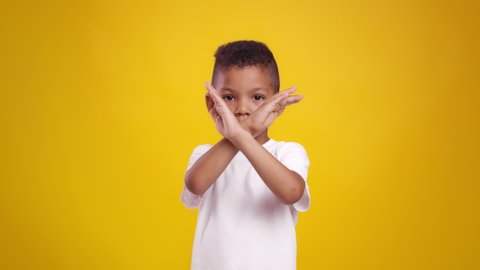 Stop kids abuse. Cute little african american boy crossing hands, showing rejection gesture to camera, posing over orange studio background, slow motion