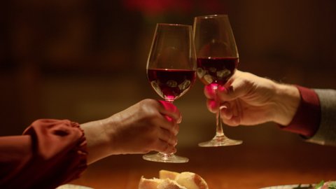 Closeup clinking wine glasses in senior couple hands. Grandparents toasting wine glasses in restaurant. Mature couple date home. Rich old people enjoy retirement time. Old aged couple romantic dinner 