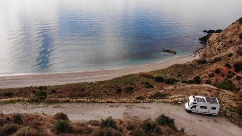 Aerial view of camper with many solar photovoltaic panels on roof camping on sea coast, andalusian cliff in Spain. Renewable free energy. Caravan vacation.