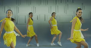 4k Group of beautiful , funny, stylish girls in yellow dresses dancing inside pavilion with grey background  . Synchronized dance of female ensemble for video clip  Woman dancers with the same outfit 