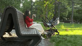 Mother with baby stroller on a walk outdoors, child sitting in gray bassinet, mom with six month old baby boy in infant kid carriage in park on a sunny summer day. High quality 4k footage