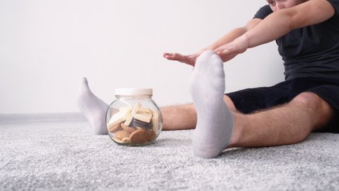 Candy man. Sport motivation. Lazy gym. Home fitness. Tired guy doing stretching bend forward with great effort getting biscuits jar in light room interior.