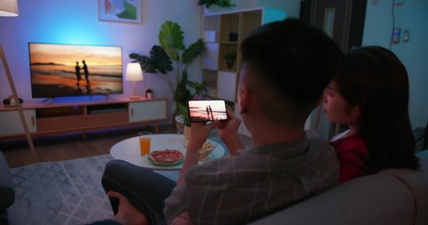 asian couple using smart phone to share content on tv in the living room at night - transfer video from smartphone to television screen