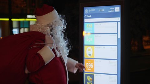 Kiev, Ukraine circa 2021: Santa Claus in traditional festive costume uses a digital citylight board on the night of Christmas Eve
