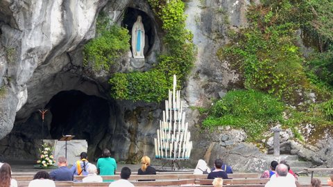 Lourdes, France - August 28, 2021: Pilgrims praying in front of the holy cave - grotto in Lourdes, the place of Marian apparitions.