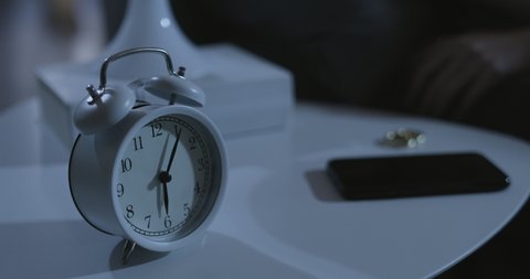 Sleepy woman turning off the alarm clock ringing on her bedside table