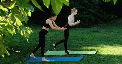 Two girls practice yoga outdoors. Yoga class is doing exercises in park. Women doing exercises warrior pose.
