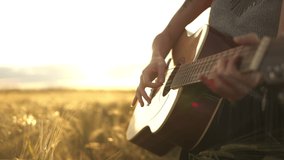Young female person playing music on acoustic guitar and singing outdoors in summer. Musician guitarist lady play in meadow field at sunset. Close-up hands. People, lifestyle, expression concept. - Powered by Shutterstock - Get 15% off with code: PIKWIZARD15