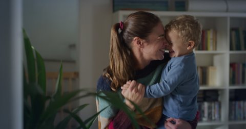 Cinematic authentic shot of young happy mother keeping in arms her toddler baby boy and having fun to dance together in living room at home. Concept of  happiness, love, childhood, life, motherhood.