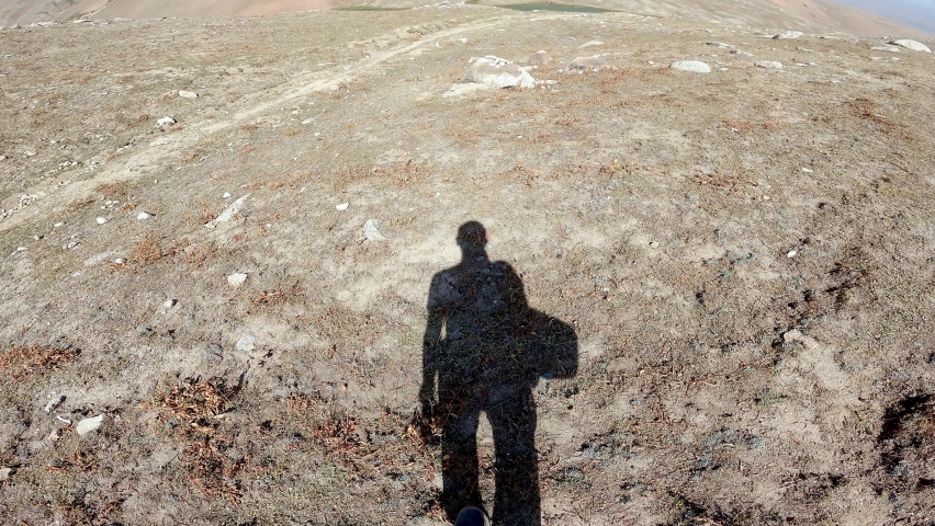The shadow of a tourist walking up a mountain and filming himself