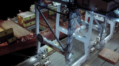 Aerial view of cargo ship with cargo containers stands on a berth in the port at the loading and unloading of containers at night time