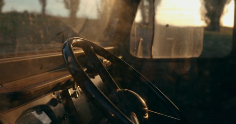 View of the interior of a vintage pickup truck through the driver's window. Instrument panel and steering wheel with the sun in backlight.
