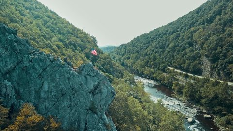 Magnificent aerial shot of rock cliff with the United States of America flag in valley with river