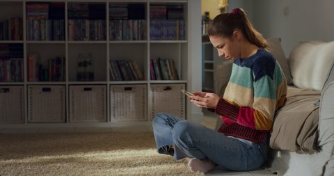Cinematic shot of young woman is using technology smartphone for work or family entertainment in living room at home. 