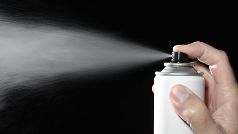 A man depresses the button on an aerosol spray can, dispensing chemicals into the atmosphere