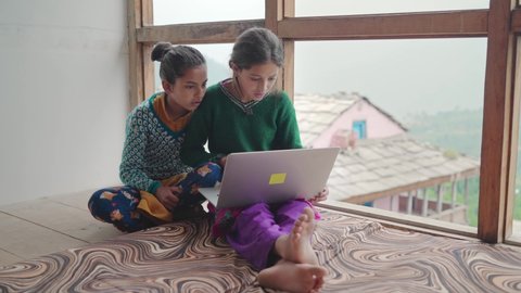 Two young village or rural school girls sitting indoors and using the laptop with the internet to study in an interior house set up with the green mountains in the back. learning and education concept