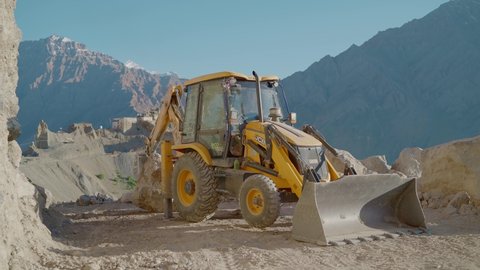  A Backhoe loader in action moving heavy rocks or boulders during the construction of the road in the mountainous region of Himalaya, Spiti Valley, Himachal Pradesh, India (October 2021)