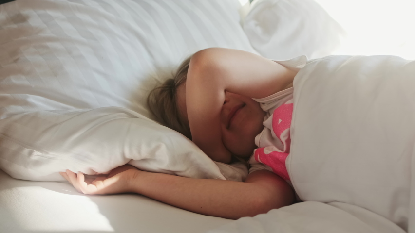Cute little girl child wakes up in the morning in bed in the bedroom on an orthopedic mattress and pillow after a healthy sleep and stretches. Royalty-Free Stock Footage #1080587711