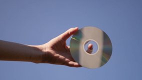 Hand holding CD disk on blue sky background. Data storage concept. Compact media disc 4k video